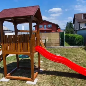 Sigurno drveno igralište za djecu s toboganom, smješteno u zelenom dvorištu pod vedrim nebom.