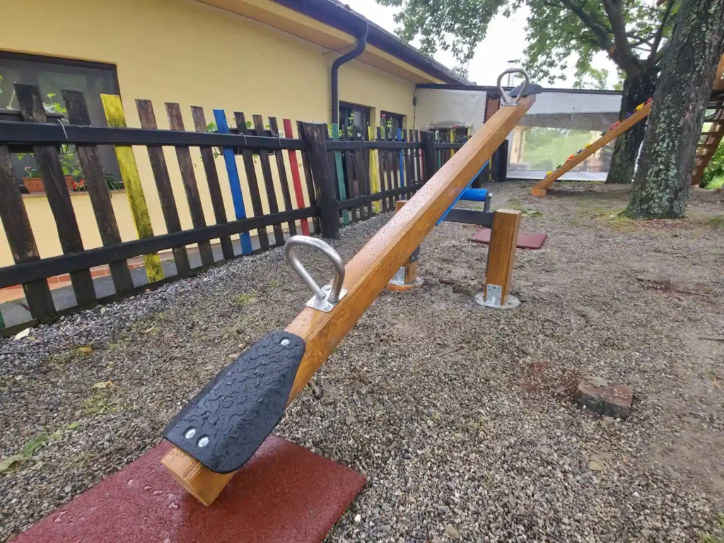 Sigurna drvena njihalica za djecu s gumenim sjedalima, smještena u ograđenom dvorištu uz zgradu.