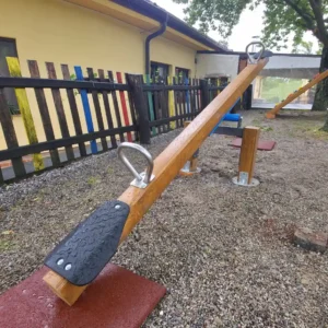 Sigurna drvena njihalica za djecu s gumenim sjedalima, smještena u ograđenom dvorištu uz zgradu.