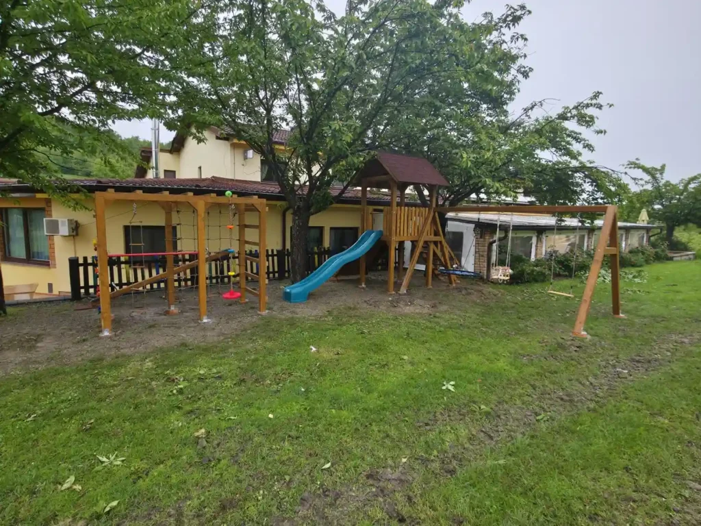 Dječje igralište s toboganom, ljuljačkama, penjalicama i užetom smješteno u dvorištu uz zgradu.
